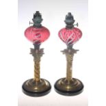 Pair of brass and cranberry oil lamps with swirled glass,