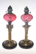 Pair of brass and cranberry oil lamps with swirled glass,