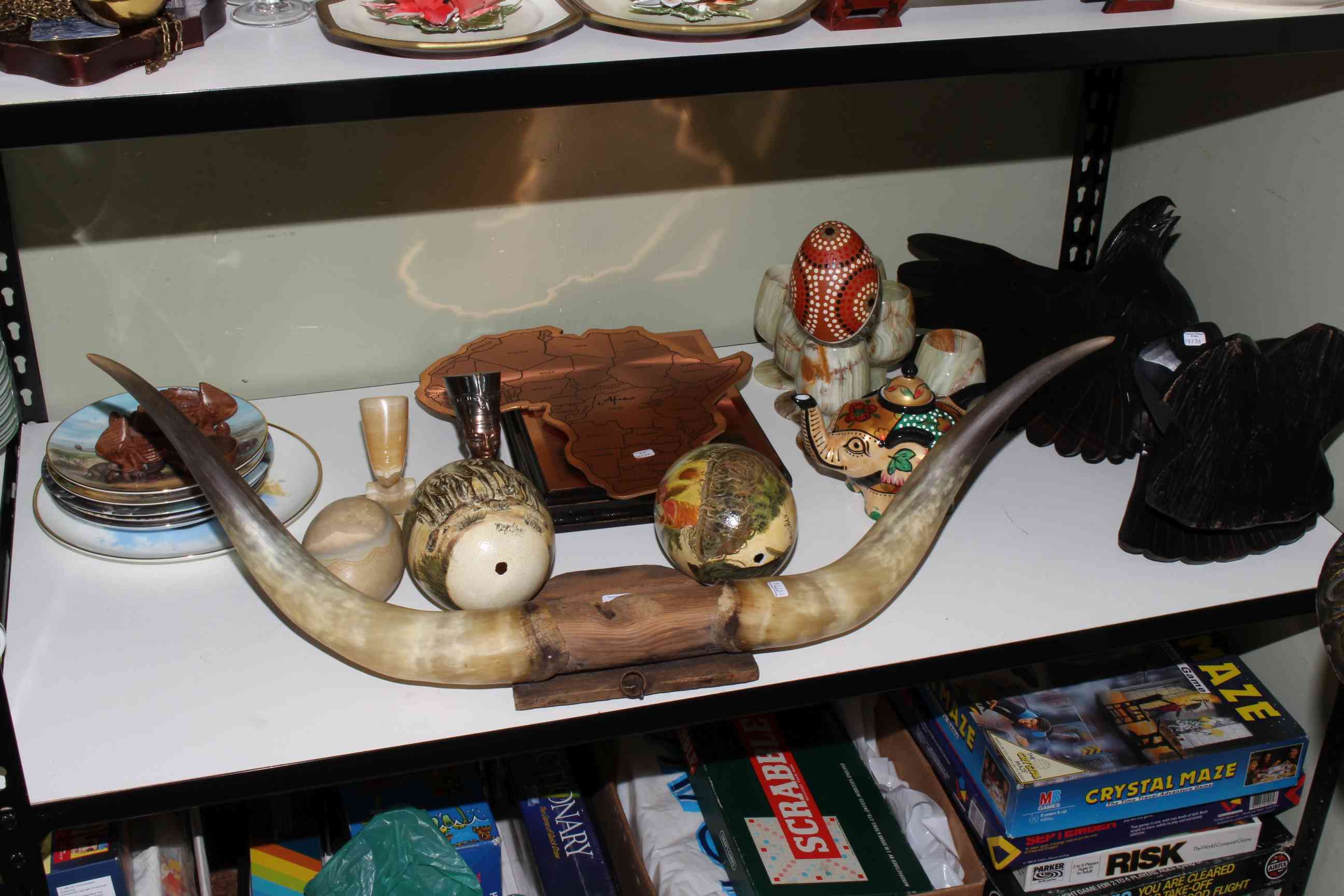 Shelf of collectables including carved eagle, mounted horns, hand-painted ostrich eggs,