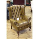 Buttoned leather wing armchair on cabriole legs.