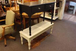 Black painted two drawer side table and rattan topped end of bed seat.
