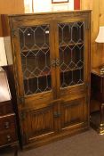 Old Charm oak bookcase with two leaded glass doors above linen fold cupboard doors.