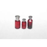 Three cranberry glass scent bottles with silver tops.