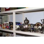 Shelf of cameras, metal wares, mantel clocks, Wade, binoculars, cutlery, glass.
