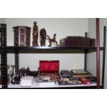 Shelf collection of presentation pack coins, metalwares, cameras, tribal wood ornaments, cutlery,