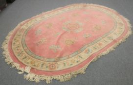 An oval embossed Chinese fringed rug on pink ground