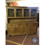A blonde oak four door kitchen dresser fitted with cupboards and drawers beneath