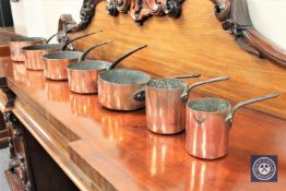 A graduated set of seven Victorian copper pans with iron handles,