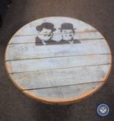 An oak barrel topped table on metal legs depicting Laurel & Hardy