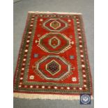 A Persian fringed rug on red ground,