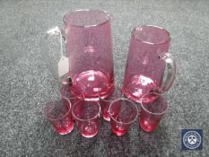 Two cranberry glass jugs together with six shot glasses