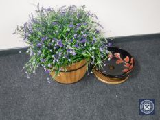 A barrel planter containing artificial plants and a black floral ceramic basin