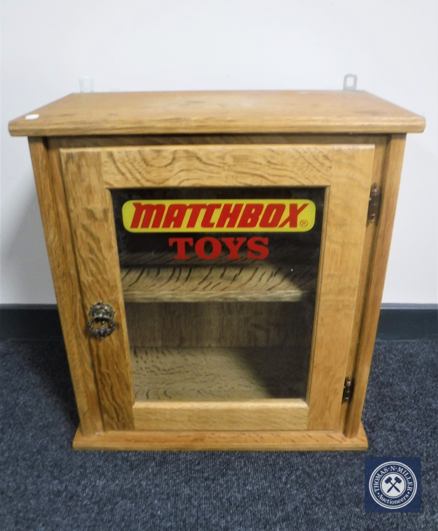 A blonde oak single door wall cabinet with "Matchbox Toys" advertising