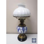 An antique continental brass oil lamp with blue and white china reservoir and white glass shade