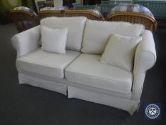 A two-seater bed settee upholstered in white fabric, with two cushions.