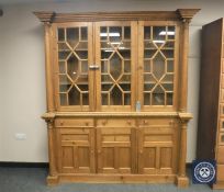 A heavily carved pine glazed inverted break fronted bookcase fitted with cupboards and drawers