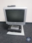 A Philips analogue television on stand with remote together with a Thompson digibox and a Sharp VCR
