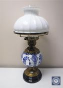 An antique continental brass oil lamp with blue and white china reservoir and white glass shade