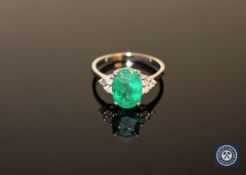 A 14ct white gold emerald and diamond ring, the oval-cut, deep-green emerald weighing 2.