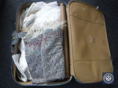 A suitcase of a fringed throw and assorted table linen