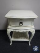 A contemporary cream bedside table fitted a drawer with wicker under shelf