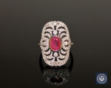 An 18ct white gold ruby and diamond cluster ring, a central oval-cut pinkish-red ruby weighing 0.