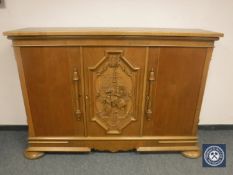 A continental carved oak triple door side cabinet on bun feet,