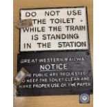 Two metal railway signs : "DO NOT USE THE TOILET WHILE THE TRAIN IS STANDING IN THE STATION" and