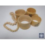 Five antique ivory napkin rings together with a beaded necklace