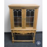 A blond oak double door cabinet with stained leaded glass panel doors
