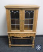 A blond oak double door cabinet with stained leaded glass panel doors