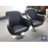 A pair of black leather swivel armchairs on chrome bases