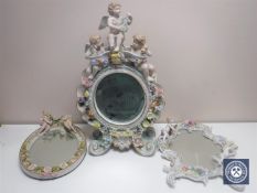 A continental porcelain encrusted mirror surmounted by cherubs together with two further similar
