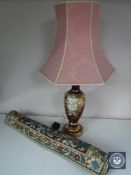 An ornate red glass table lamp with shade and a hanging tapestry