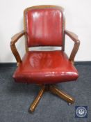 An Edwardian oak swivel office desk chair upholstered in a red buttoned leather