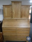 An antique pine bureau fitted with four drawers and cupboards above