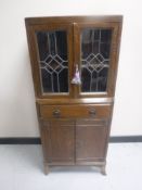 An Edwardian oak cabinet with leaded glass doors fitted a drawer and cupboards beneath