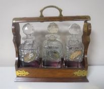 An Edwardian oak three bottle Tantalus with brass mounts and five decanter labels