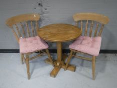 A circular oak pedestal table together with two kitchen chairs