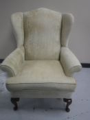 A 20th century wingback armchair upholstered in a cream fabric