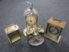 A Schatz anniversary clock under shade together with two mantel clocks and an alarm clock