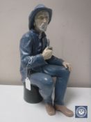 A Nao figure of a fisherman seated smoking a pipe in a matt finish,