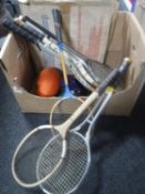 A box containing assorted tennis rackets, dart board, rugby ball,