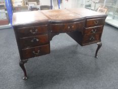An Edwardian mahogany shaped front writing desk fitted nine drawers with brown leather tooled inset