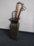 A metal wicker stick stand containing seven assorted walking sticks