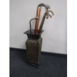 A metal wicker stick stand containing seven assorted walking sticks