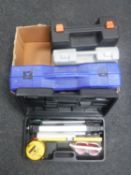 A box of cased tile cutter, cased laser level, soldering iron,