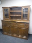 An early 20th century oak leaded door dresser fitted cupboards and drawers beneath