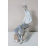 A Lladro figure of a man seated on a rock reading a book