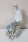 A Lladro figure of a man seated on a rock reading a book